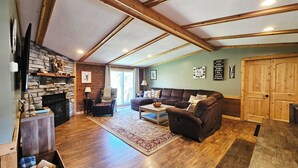 A spacious living room with a fireplace, wooden beams, a sofa, a coffee table, and a large wooden door.