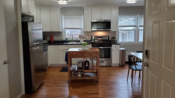 A modern kitchen with white cabinets, stainless steel appliances, a wooden island, and a view of the outside through the windows.