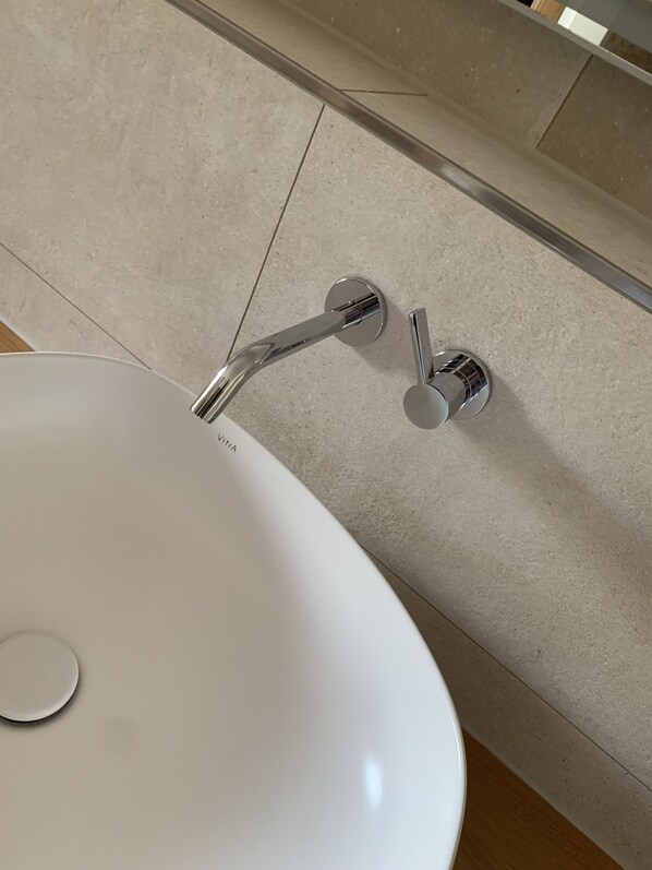 Een witte wastafel met een chromen kraan en een spiegel erboven.