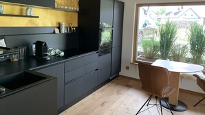 A modern kitchen with dark cabinetry, a built-in oven, and a window overlooking a garden. - Small black forest lodge (Efringen-Kirchen)