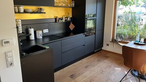 A modern kitchen with black cabinets, a wooden countertop, and a window with a view of greenery. - Small black forest lodge (Efringen-Kirchen)