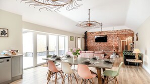 A modern dining area with a brick wall, a flat-screen TV mounted on the wall, and a unique ceiling light fixture. - Cattle Crush Cottage - UK35988 (Skerne, near Driffield)
