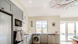 A modern kitchen with grey cabinetry, a built-in oven, a washing machine, and a dining area with a table and chairs. - Cattle Crush Cottage - UK35988 (Skerne, near Driffield)