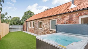 A backyard with a hot tub, a brick house, and a green lawn. - Cattle Crush Cottage - UK35988 (Skerne, near Driffield)