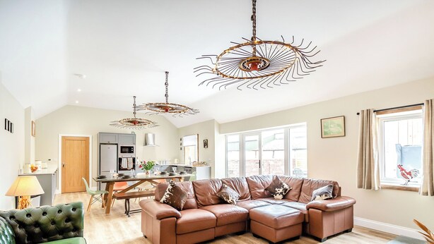 A spacious living room with a sectional sofa, a green armchair, and a dining area with a table and chairs. - Cattle Crush Cottage - UK35988 (Skerne, near Driffield)