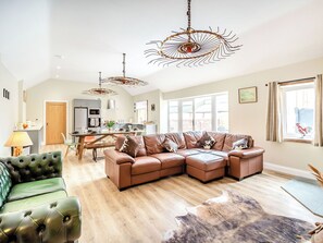 A spacious living room with a sectional sofa, a green armchair, and a dining area with a table and chairs.