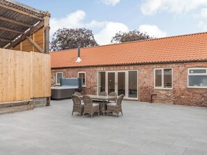 A patio area with a brick building, a wooden fence, and a hot tub. - Cattle Crush Cottage - UK35988 (Skerne, near Driffield)