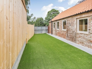 A backyard with a wooden fence, a brick building with windows, and a well-maintained lawn.