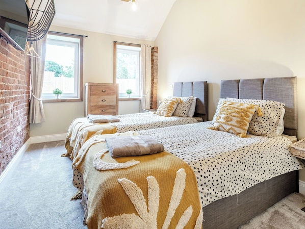 A bedroom with a brick wall, a wooden dresser, two beds with patterned bedding, and a window with curtains.