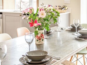 A dining table set with plates, bowls, and wine glasses, a vase with flowers, and a window in the background. - Cattle Crush Cottage - UK35988 (Skerne, near Driffield)