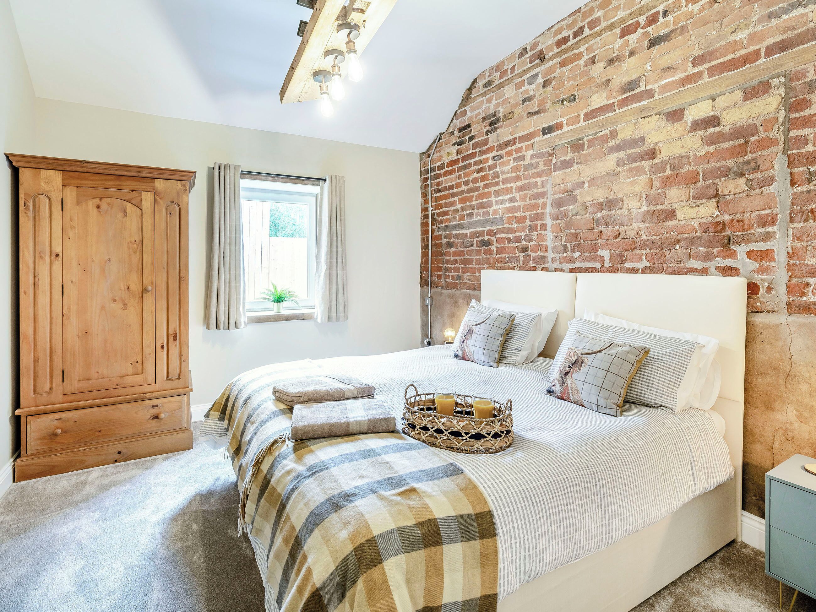 A bedroom with a large bed, a wooden wardrobe, a brick wall, and a window with curtains.