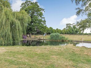 A serene park with a pond, trees, and playground equipment.