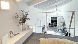A modern interior with a sofa, a fluffy rug, a plant, and a mirror reflecting a staircase and dining area. - Unique Flat (Athens)