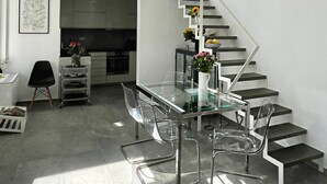 A modern kitchen with a glass dining table and chairs, a staircase, and a view of the sky through the windows. - Unique Flat (Athens)