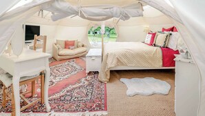 A tented accommodation with a bed, a small desk, a chair, and a television.
