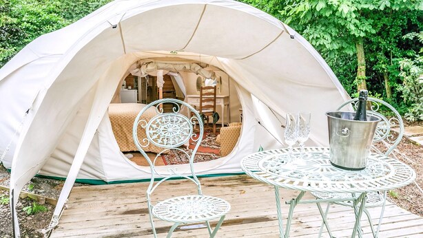 A tent with a bed, a table with chairs, and a bottle of champagne.