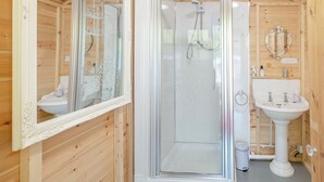 A wooden cabin bathroom with a glass-enclosed shower, a pedestal sink, and a large mirror.