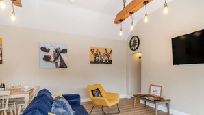 A living room with a blue sofa, a yellow armchair, and a dining area with a table set for two. - Dip Tub Den - UK35989 (Skerne, near Driffield)