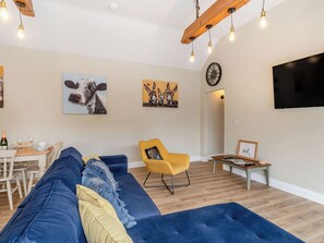 A living room with a blue sofa, a yellow armchair, and a dining area with a table set for two.