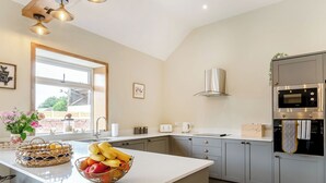 A modern kitchen with a large island, grey cabinets, stainless steel appliances, and a window providing natural light. - Dip Tub Den - UK35989 (Skerne, near Driffield)