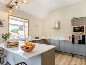 Une cuisine moderne dotée d’un grand îlot central, de meubles gris, d’appareils électroménagers en acier inoxydable et d’une fenêtre qui laisse entrer la lumière naturelle.