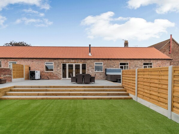 A brick house with a red-tiled roof, a patio with outdoor furniture, and a wooden fence. - Dip Tub Den - UK35989 (Skerne, near Driffield)