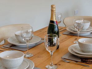 A dining table set with white ceramic plates, bowls, and wine glasses. A bottle of champagne is placed in the center. - Dip Tub Den - UK35989 (Skerne, near Driffield)