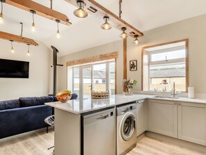 Une cuisine compacte dotée d’un lave-linge intégré, d’un canapé bleu et de luminaires suspendus.