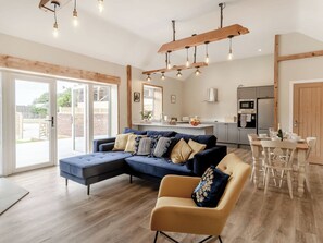 A modern living room with a sectional sofa, a small armchair, and a dining table with chairs. There is a kitchen area with a refrigerator, oven, and sink. - Dip Tub Den - UK35989 (Skerne, near Driffield)