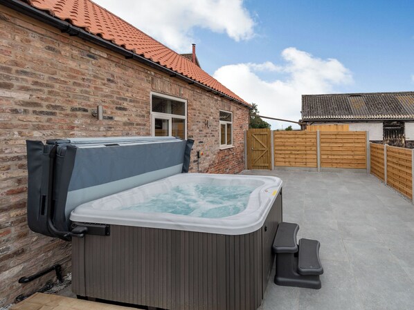 A hot tub in a backyard with a brick house and wooden fence.