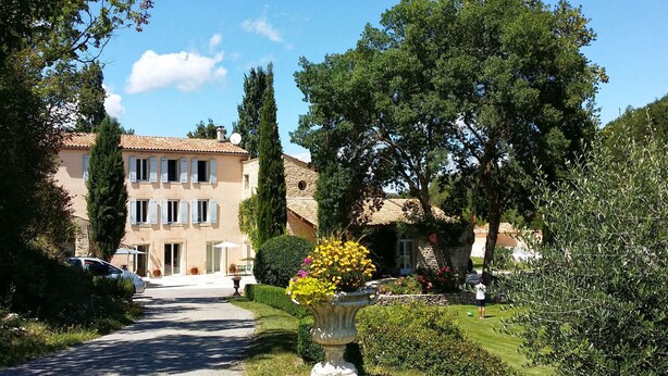 Eine Villa mit gepflasterter Auffahrt, ein Garten mit einer großen Blumenvase und einem strahlend blauen Himmel.