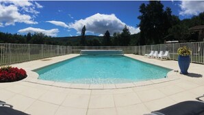 Ein rechteckiger Pool mit einer gefliesten Liegefläche, umgeben von einem weißen Zaun, und eine Reihe weißer Liegestühle an einer Seite.