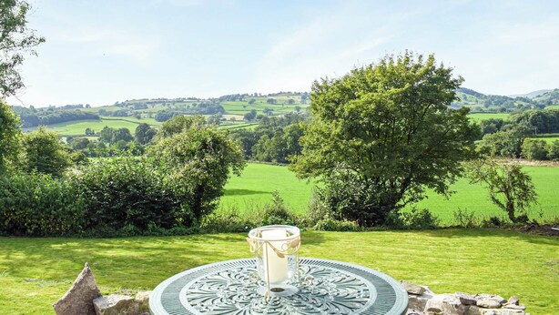 A table with a glass of water in a scenic outdoor setting with a view of rolling hills and trees. - 1 bedroom accommodation in Llansilin, near Oswestry (Llansilin, near Oswestry)