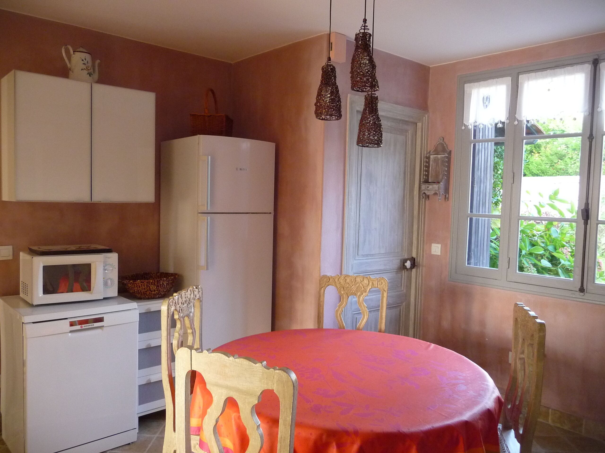 Een keuken met een magnetron, koelkast en een eettafel met stoelen.