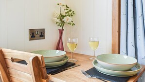 Een eettafel met twee groene borden, twee wijnglazen, een bloevas en een houten stoel.