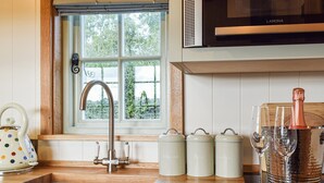 Een keuken met een RVS spoelbak, een raam met uitzicht op groen, en drie witte voorraadpotten met de tekst 'Suiker', 'Thee' en 'Koffie'.
