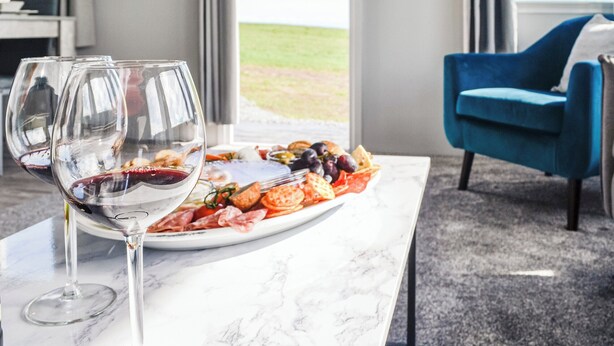 Een eettafel met een plateau visgerechten en wijnglazen, een blauwe stoel, en uitzicht op het buiten.