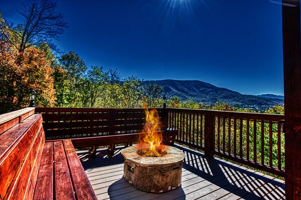 A wooden deck with a fire pit and a bench, overlooking a mountainous landscape.