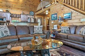 A cozy living room with a brown leather sofa, a glass coffee table, and a wooden staircase.
