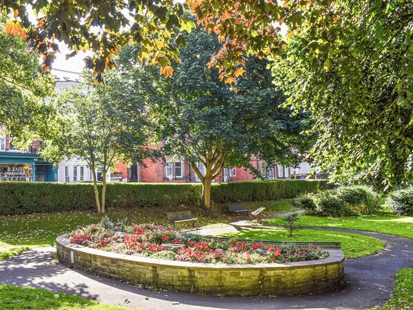 A park with a circular flower bed, benches, and a hedge.