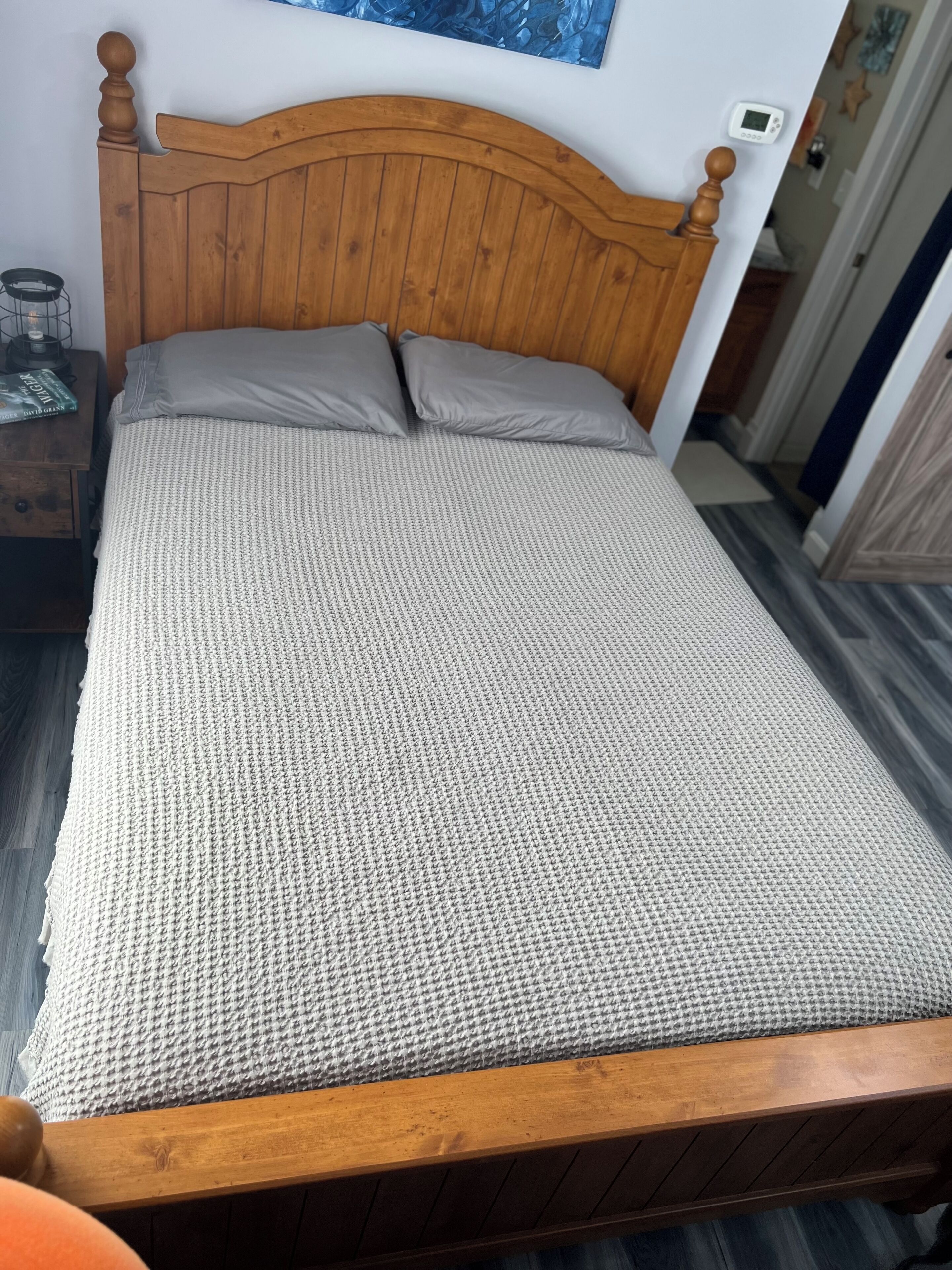 A wooden bed with a headboard, grey pillows, and a grey textured bedspread.