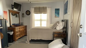 Une chambre à coucher avec un lit, une commode, un miroir, une fenêtre avec des rideaux et une porte.