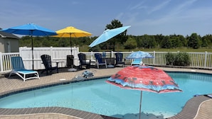 Une piscine entourée d’une terrasse en bois et d’une clôture blanche, avec des chaises longues et des parasols à proximité.
