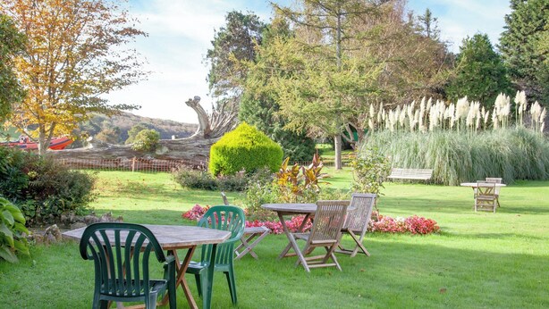 A garden with a wooden table and chairs, surrounded by greenery and a fence. - 5 bedroom accommodation in Kingsbridge (Kingsbridge)