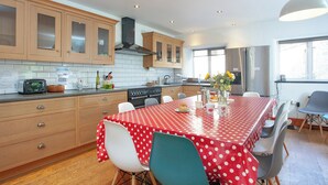 A modern kitchen with wooden cabinets, a stove, and a dining area with a red polka dot tablecloth. - 5 bedroom accommodation in Kingsbridge (Kingsbridge)