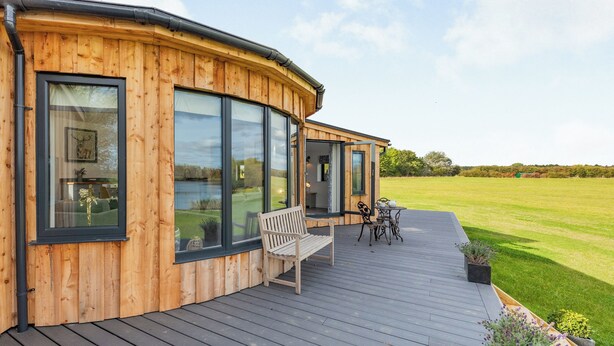 A wooden cabin with large windows, a deck, and a view of a green field. - 1 bedroom accommodation in Hawton, near Newark (Hawton, near Newark)