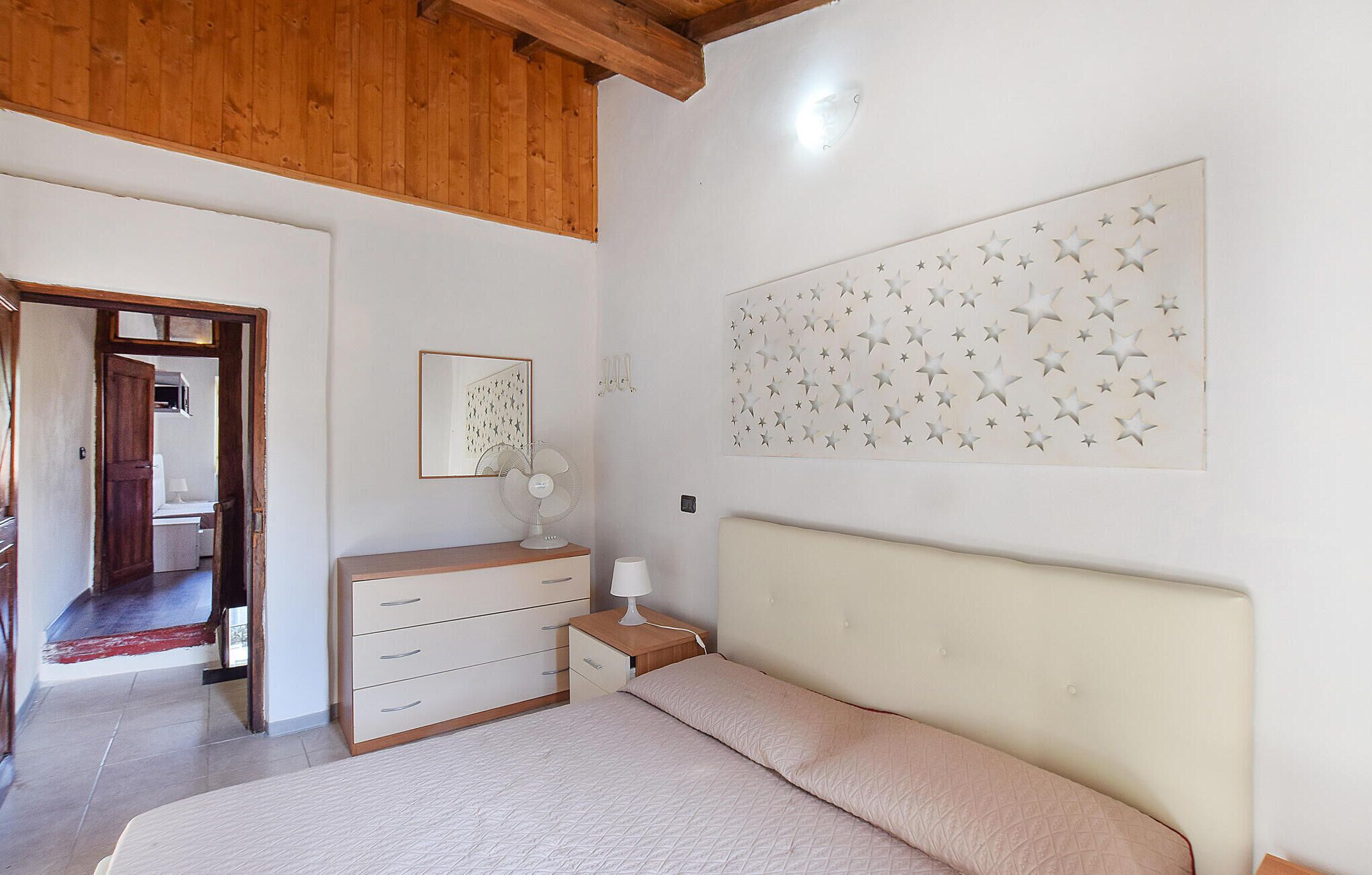 A bedroom with a bed, a dresser, a nightstand, a wall-mounted fan, and a star-patterned wall decoration.