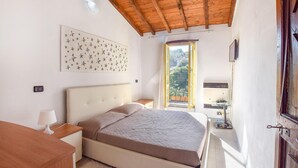 Une chambre à coucher comprenant un lit, une table de chevet, une lampe, un mur décoré de motifs d’étoiles, une fenêtre donnant sur un paysage verdoyant et un plafond en bois.