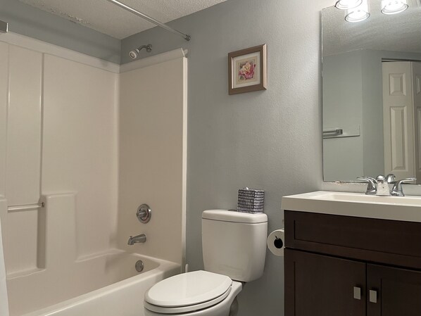 A bathroom with a bathtub, toilet, and vanity with a mirror.
