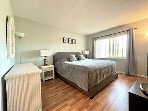 A bedroom with a bed, nightstands, a lamp, a wicker chair, and a window with curtains. - Shorewalk The Palm Condo 2Bed/2Bath Close to IMG / Beach (Bradenton)